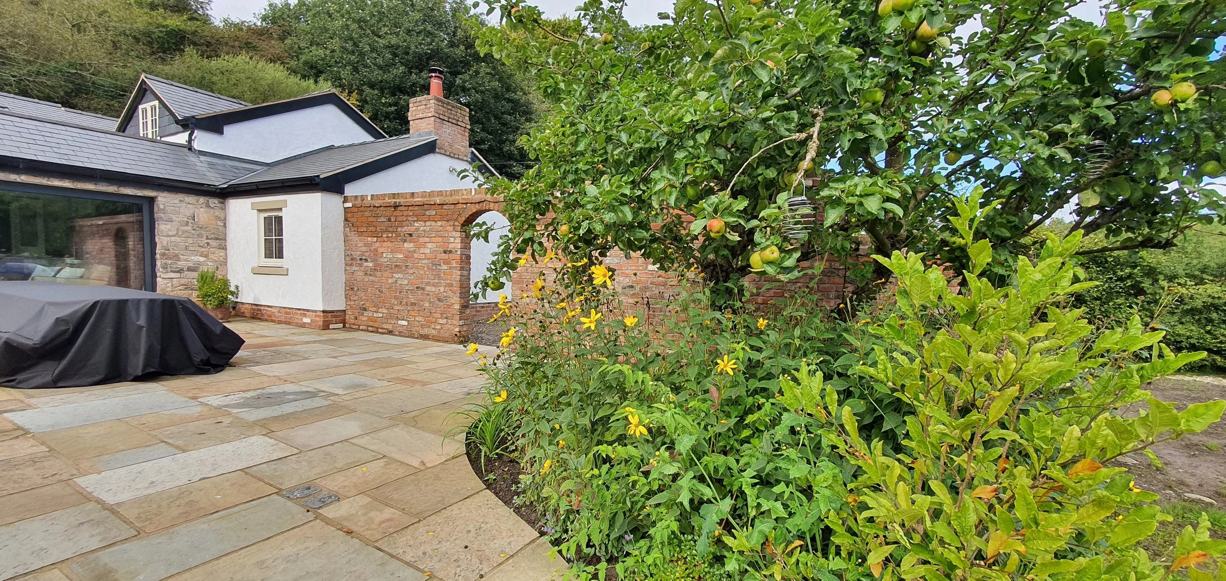 Outdoor dining area in Mold garden with brick wall and informal planting