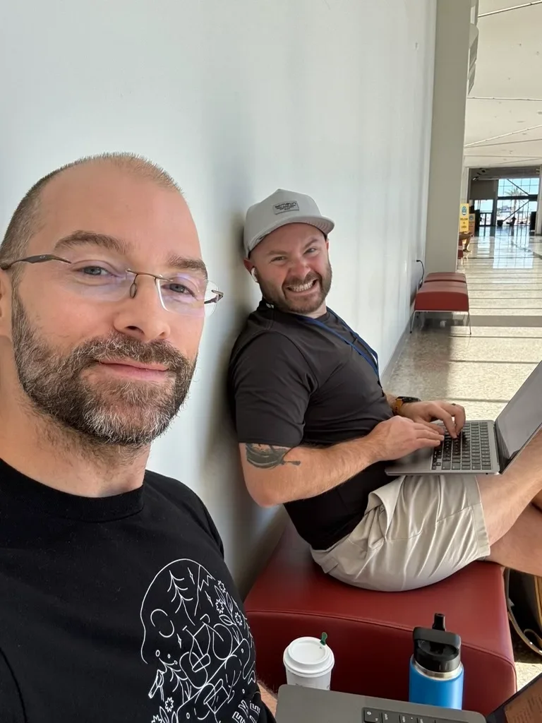 Two Ikeono team members smiling while working on laptops at a trade show venue