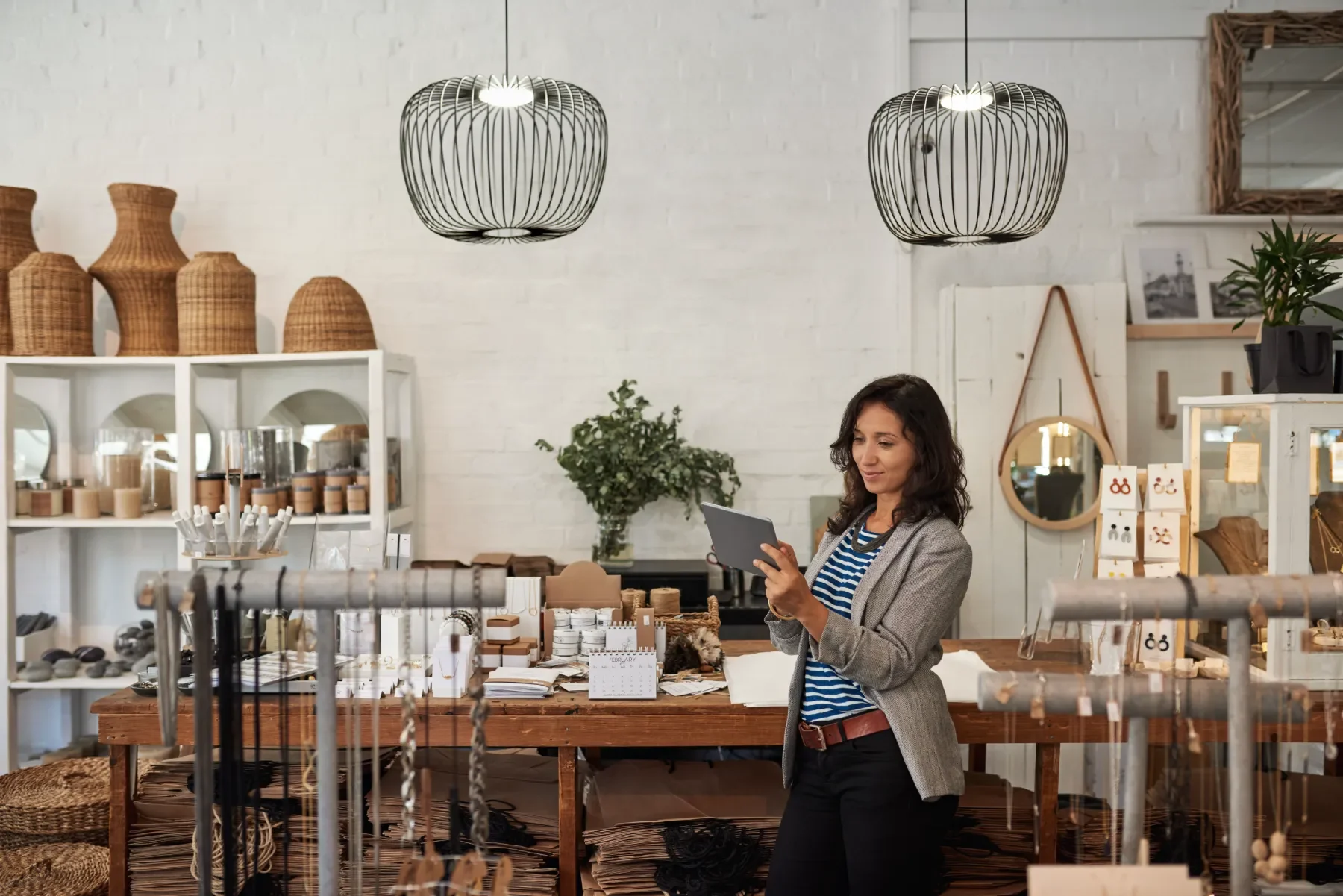 Boutique owner checking a tablet in her shop, surrounded by woven baskets and jewelry displays