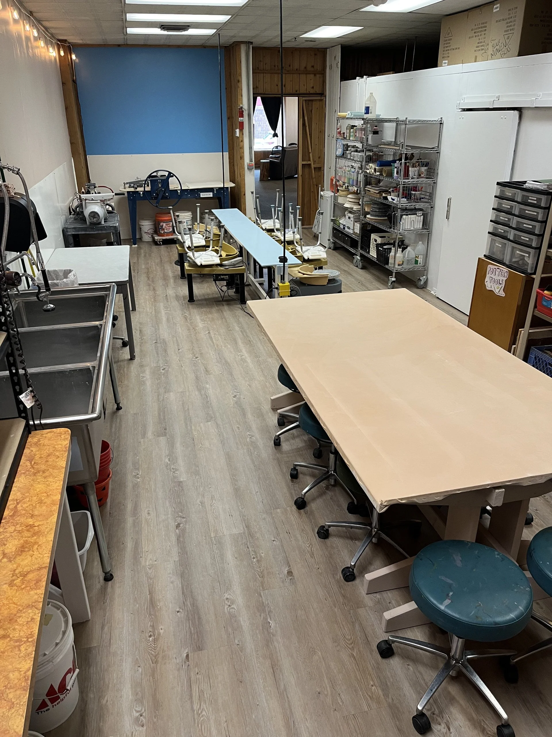 A long view down the clay studio with pottery wheels, worktables, and shelves of glaze