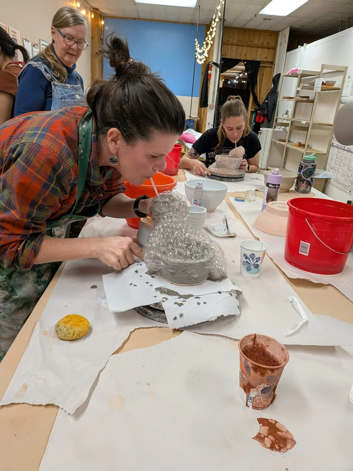 A student blowing bubble glaze onto a pot during a clay class