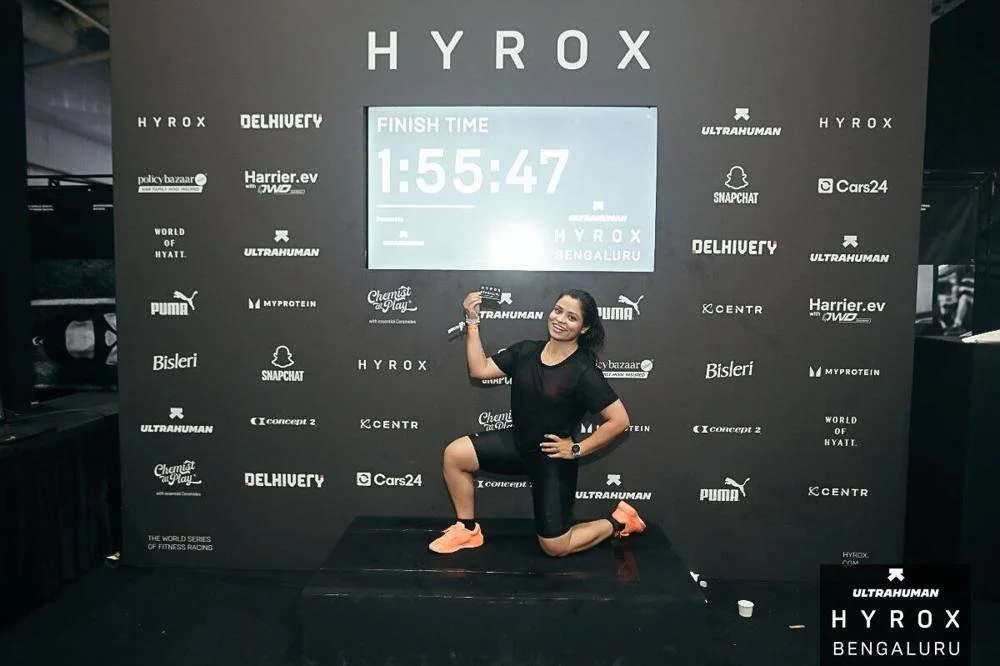 Fitness Bootcamp client at the HYROX Bengaluru finish board showing 1:55:47