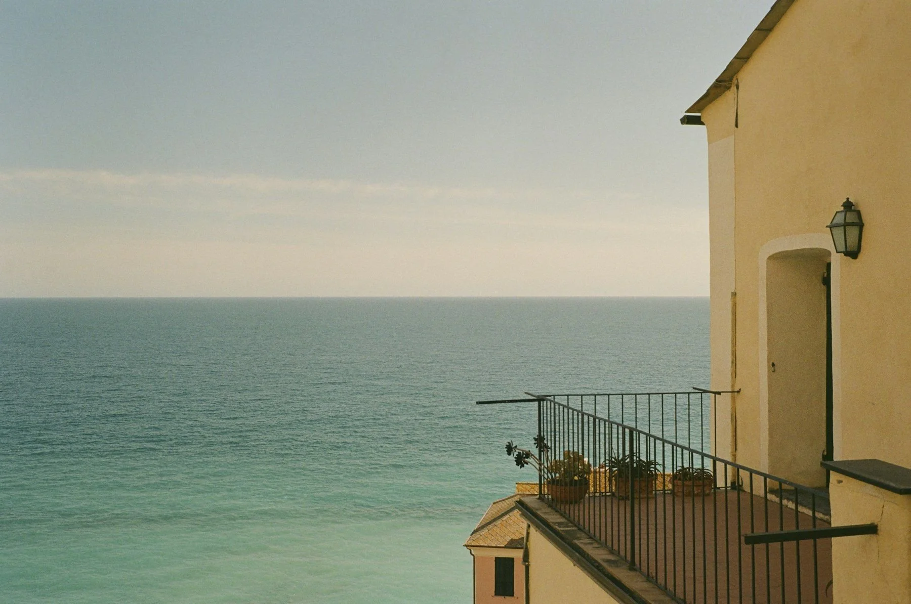 A balcony on an ochre house looking out over a calm sea