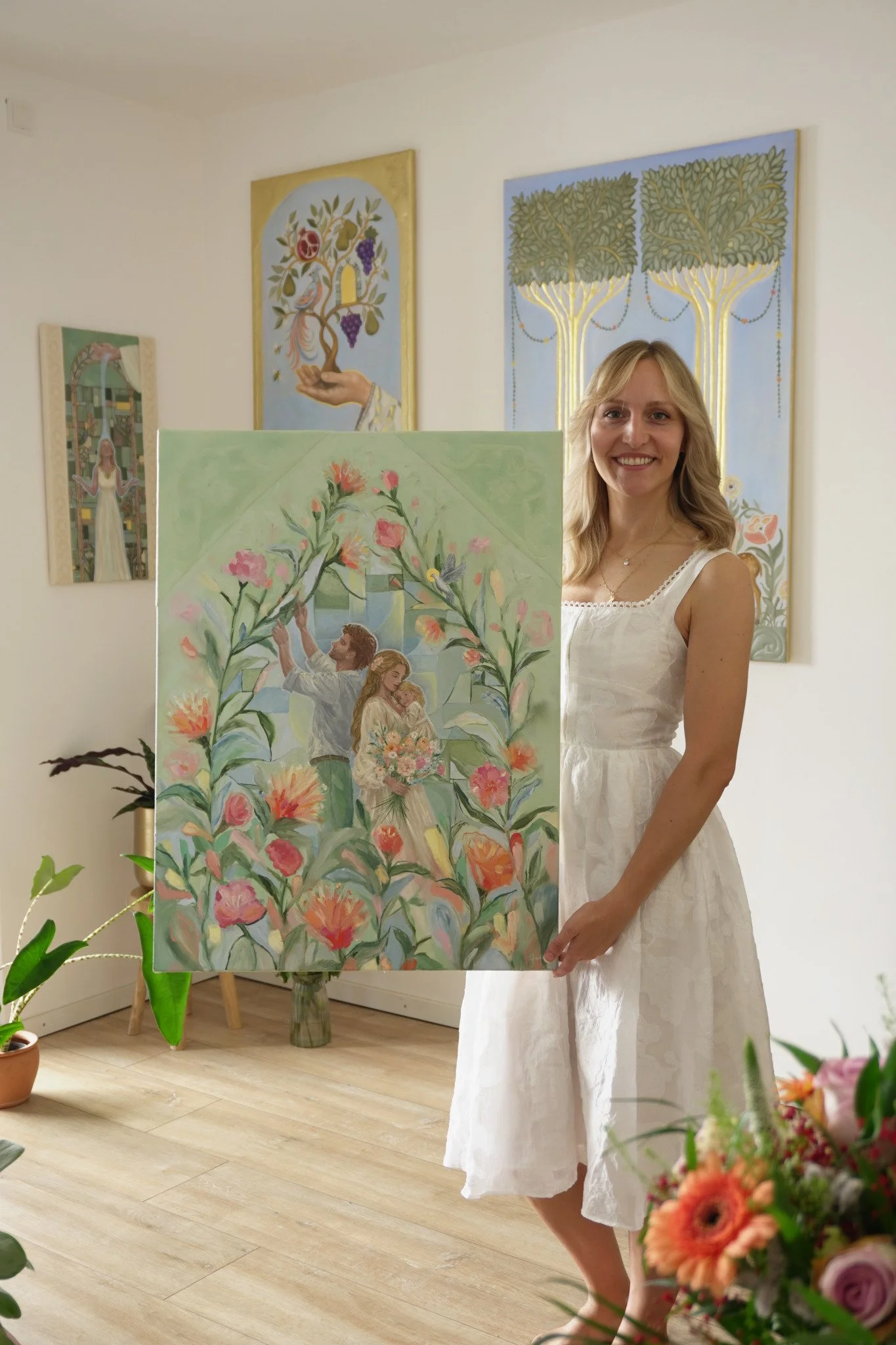 Natalie Ingerle steht in ihrem Atelier neben dem Gemälde Welcome Home mit dem Paar im Blütenbogen und hält es am rechten Bildrand