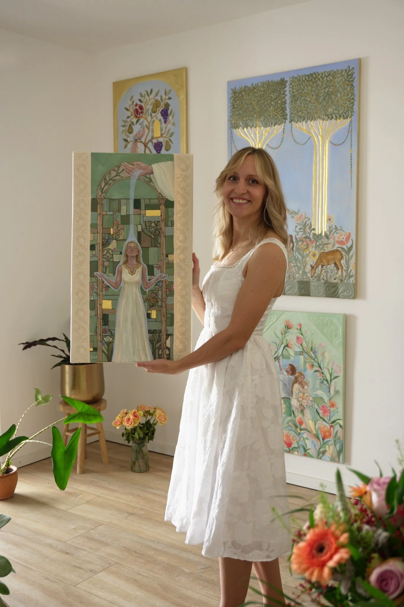Natalie Ingerle hält in ihrem Atelier das hochformatige Gemälde Aus Jesu Hand mit beiden Händen vor sich, auf dem eine Frau unter einem grünen Glasfensterbogen die Arme öffnet