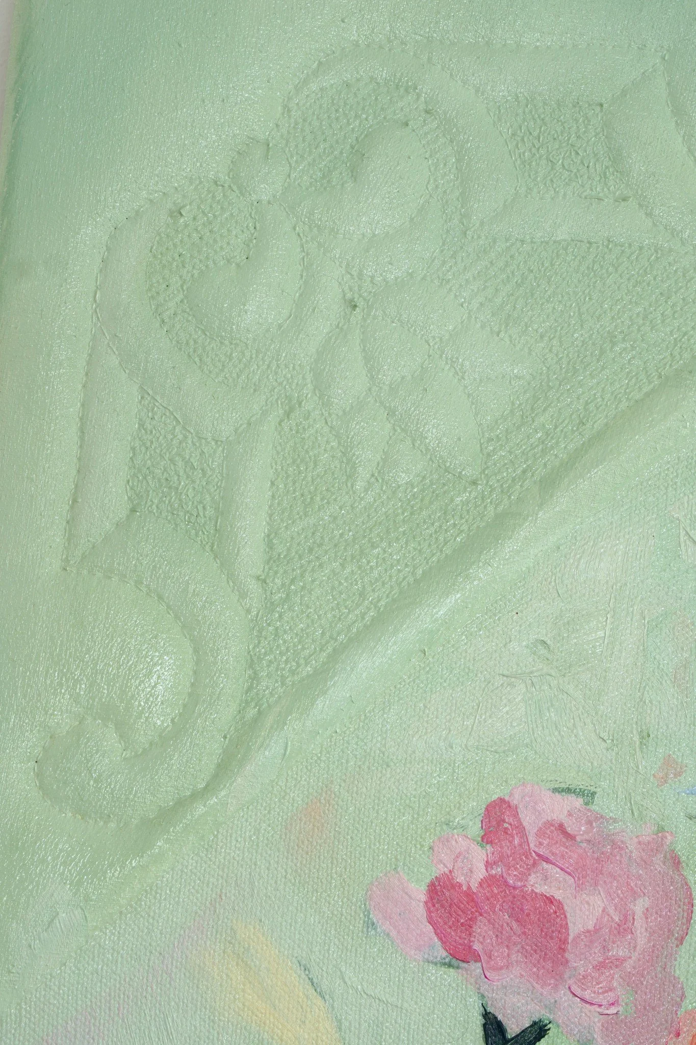 Der geprägte Giebel ganz nah: das genähte Ornament tritt als Relief aus der salbeigrünen Fläche, rechts unten eine rosa Blüte.