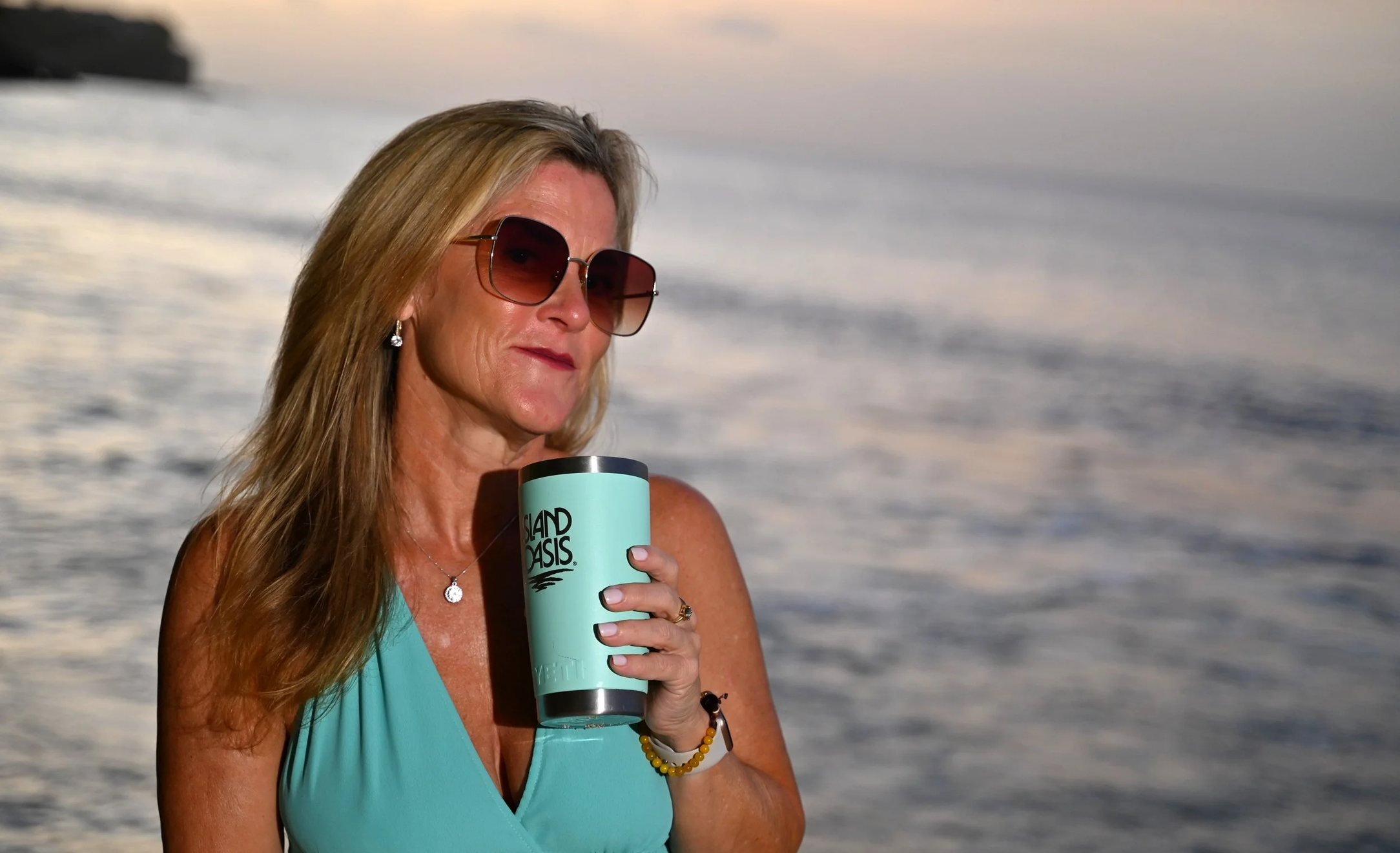 Joey Torkelson on the beach at sunset with an aqua tumbler that matches her dress