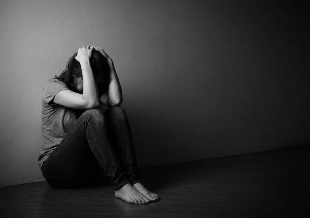 Person sitting on the floor against a wall with their head in their hands