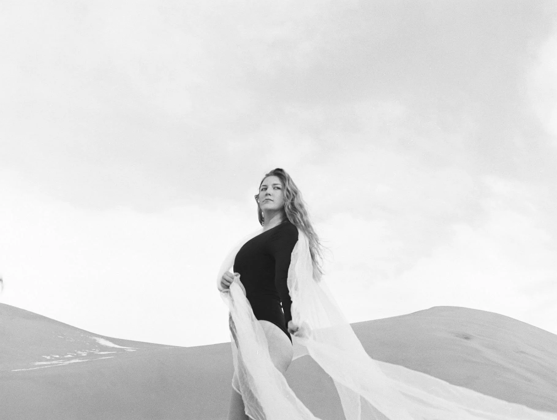 Black and white photo of a woman in the desert with white fabric flowing in the wind, creative portrait photography.