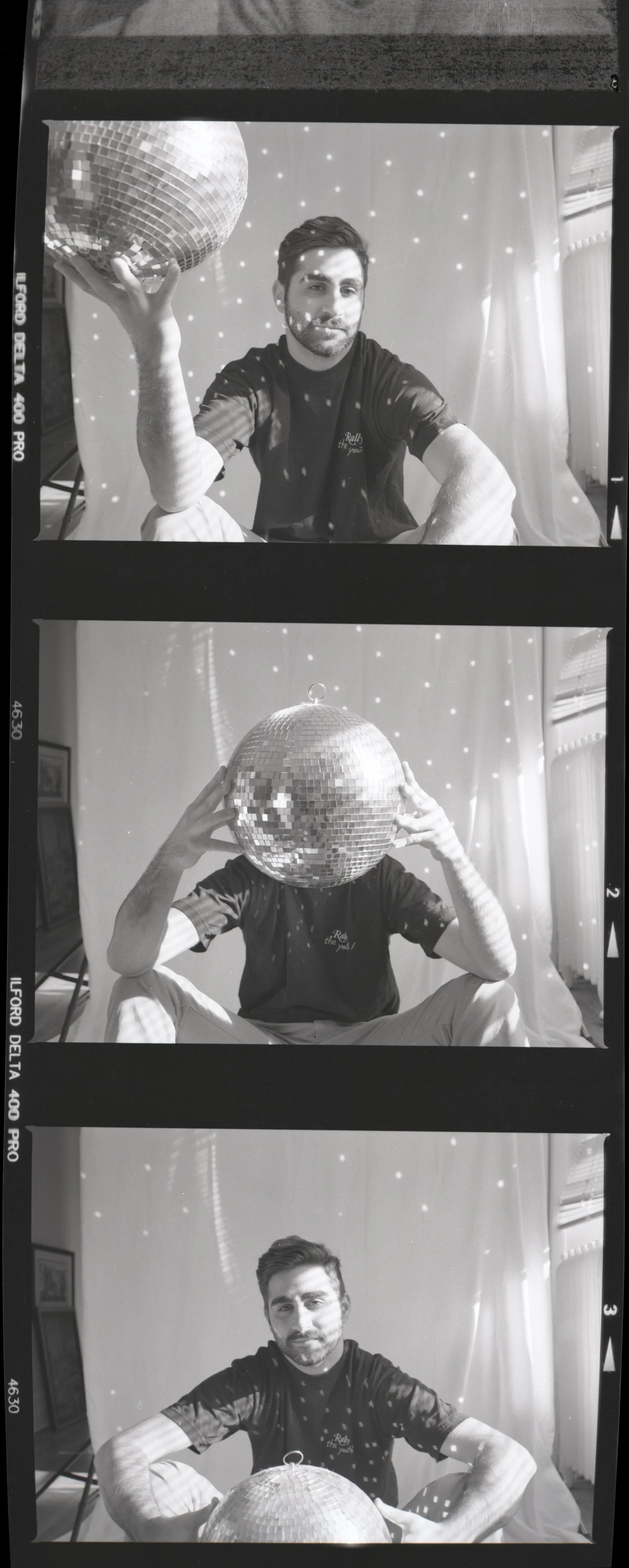 Black and white film strip photo of a man sitting in a studio with a disco ball overhead, creative portrait session.