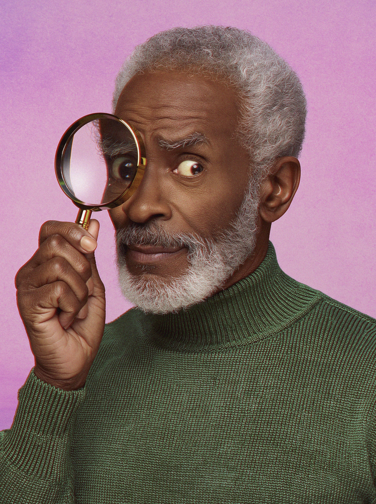 A bearded man peers through a magnifying glass