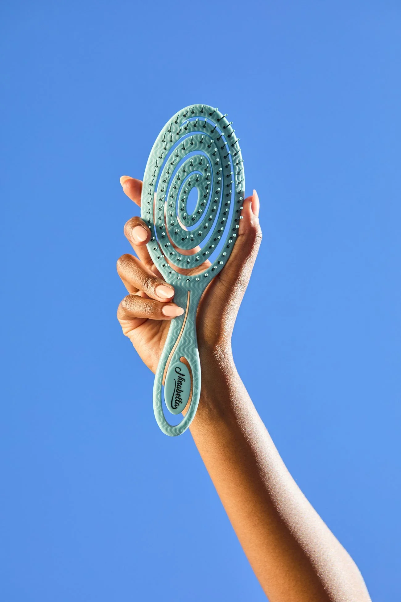 A hand holding the Ninabella spiral brush against cobalt blue
