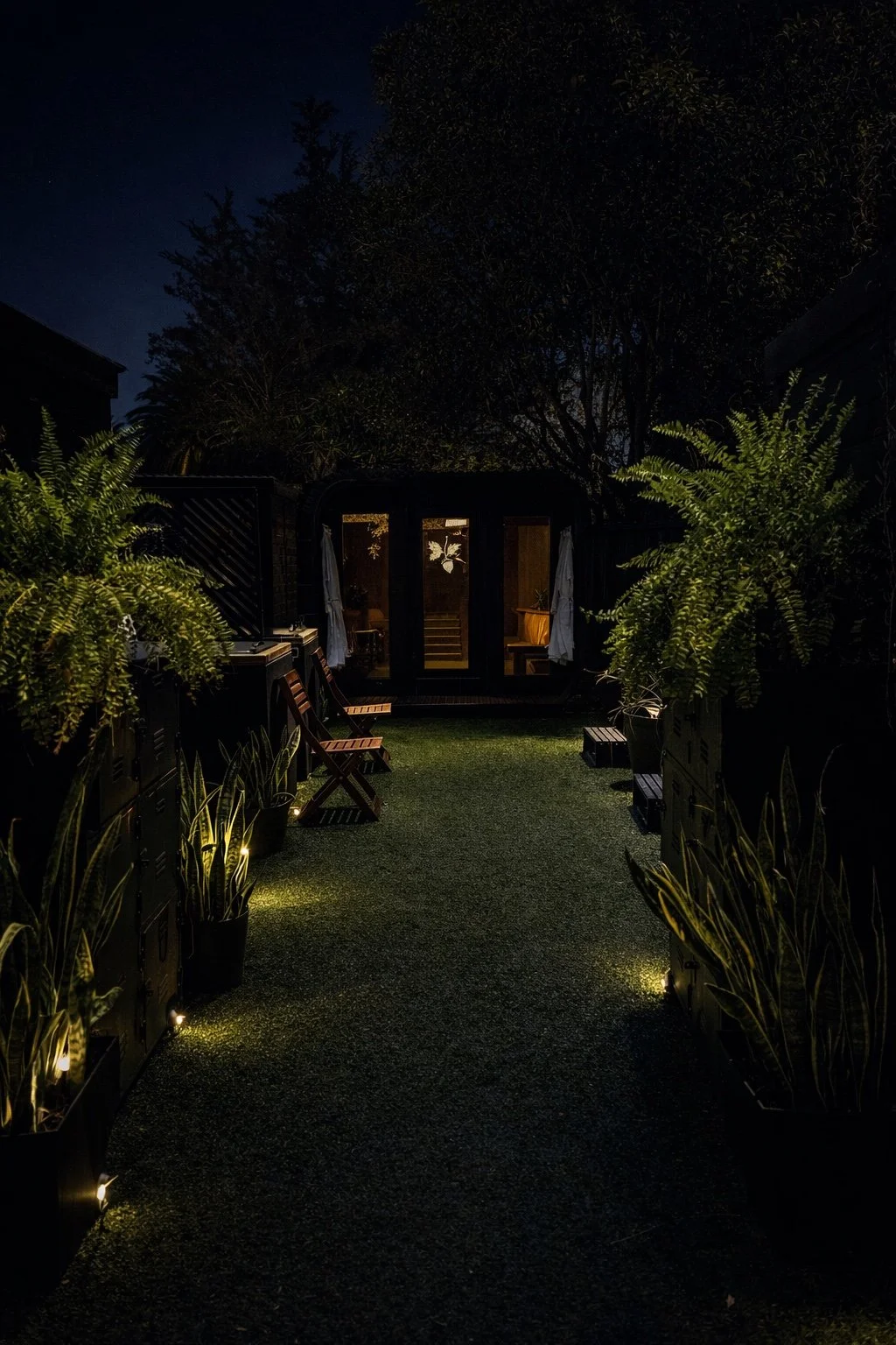 The Acorn & Oak garden at night, with softly lit greenery and the warm glow of the sauna.