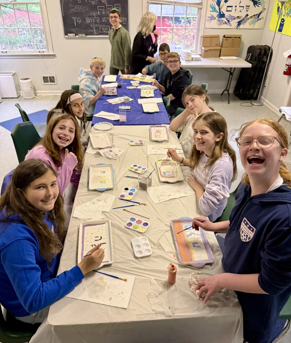 Teenagers laughing around a table during a Hebrew School activity.