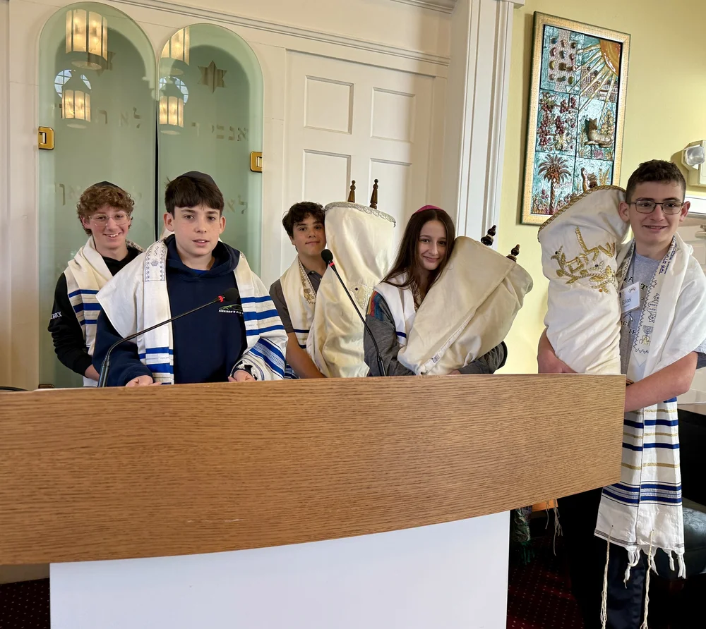 Seventh graders in tallitot at the podium, several holding Torah scrolls.