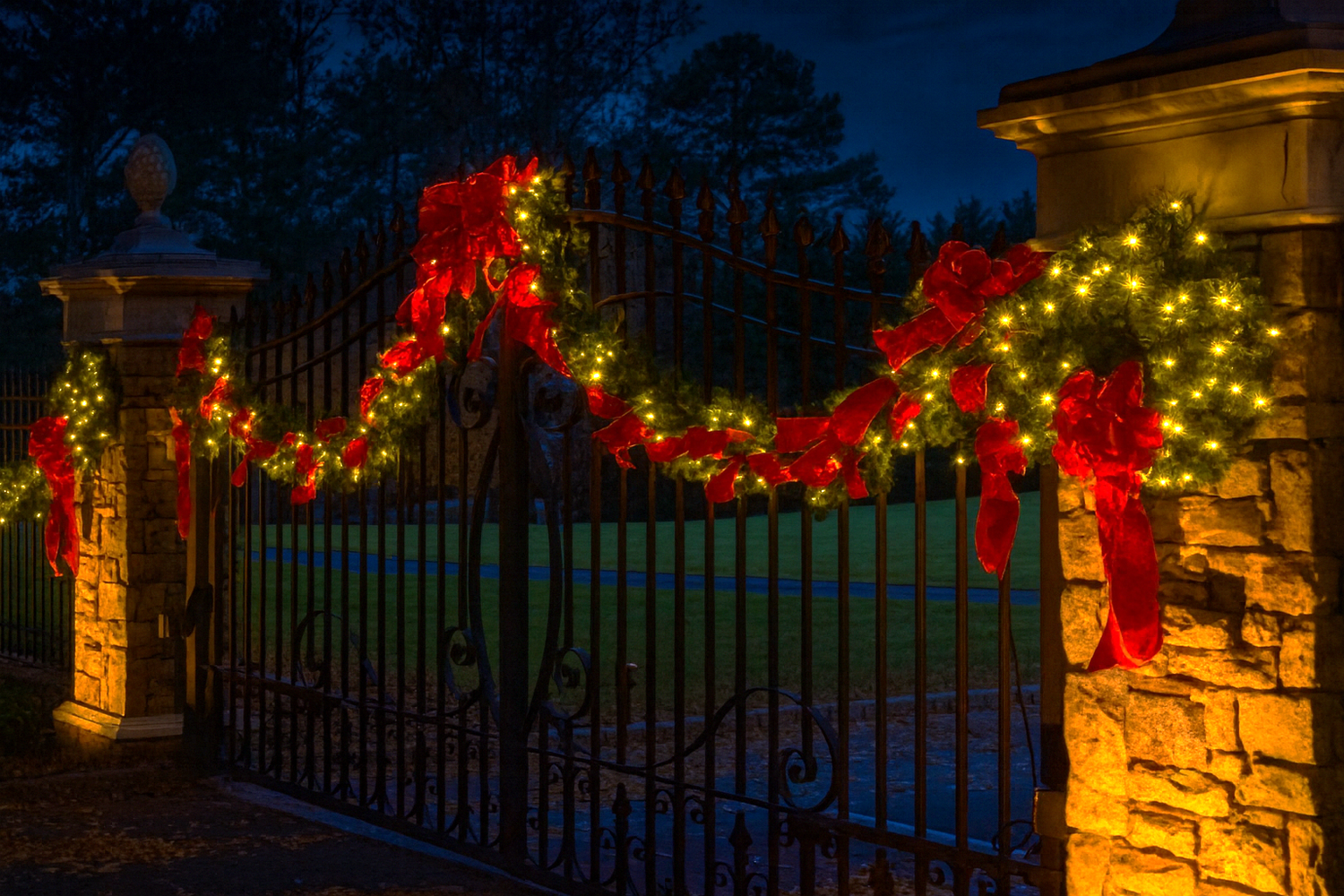 Holiday garland, red bows and warm white lighting decorating an elegant entrance gate