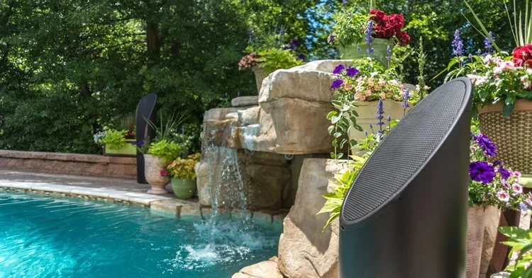 Discreet premium outdoor speaker beside a landscaped swimming pool and waterfall