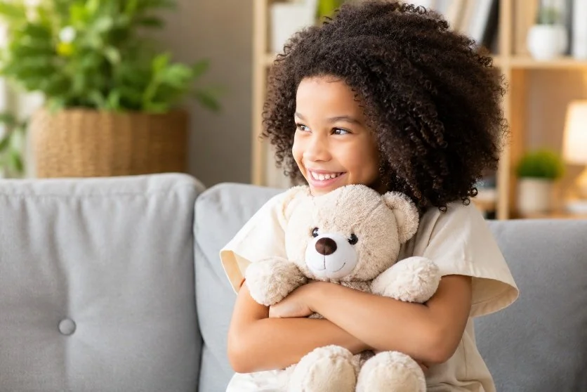 Child smiling while holding a teddy bear in a comfortable room