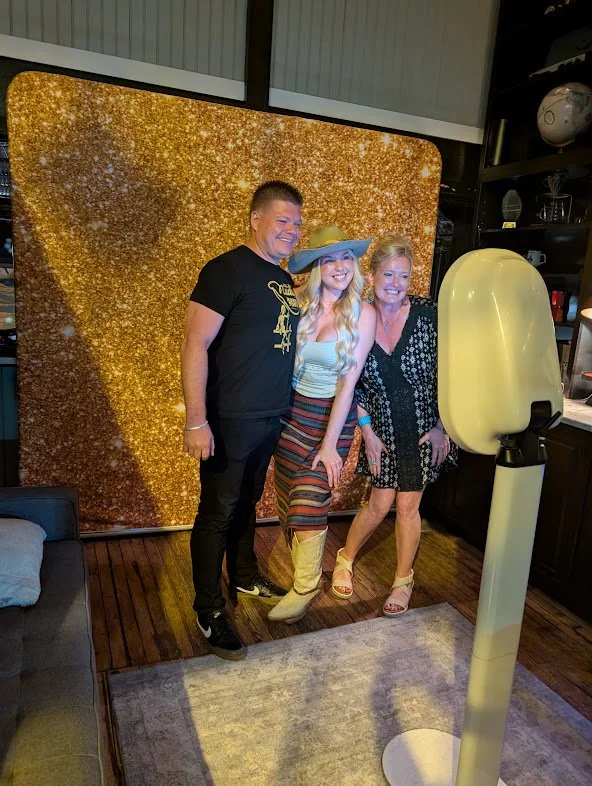 Guests posing with an artist at the Black Iris photo booth against a gold backdrop