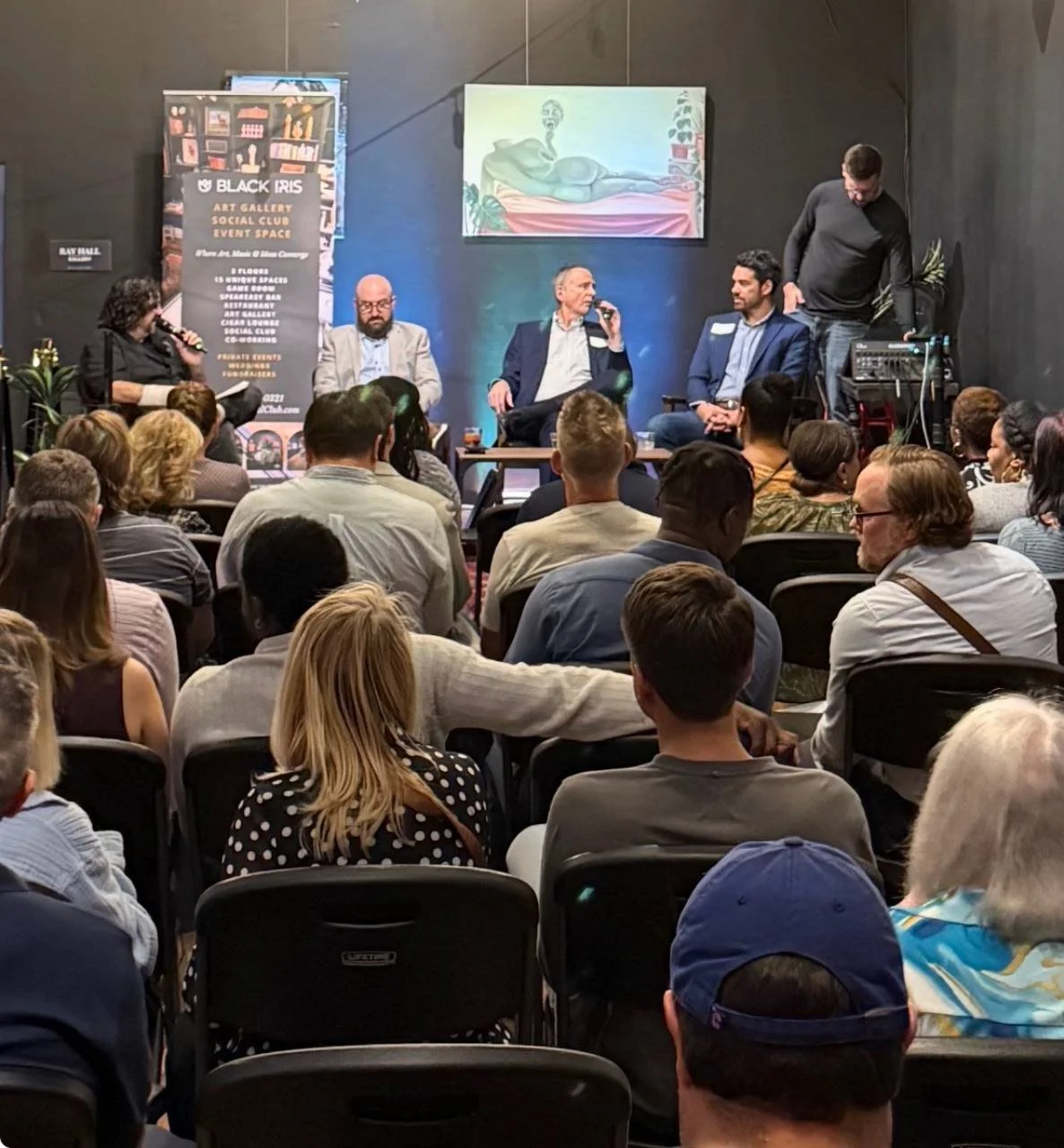 A seated audience watches a panel discussion at Black Iris
