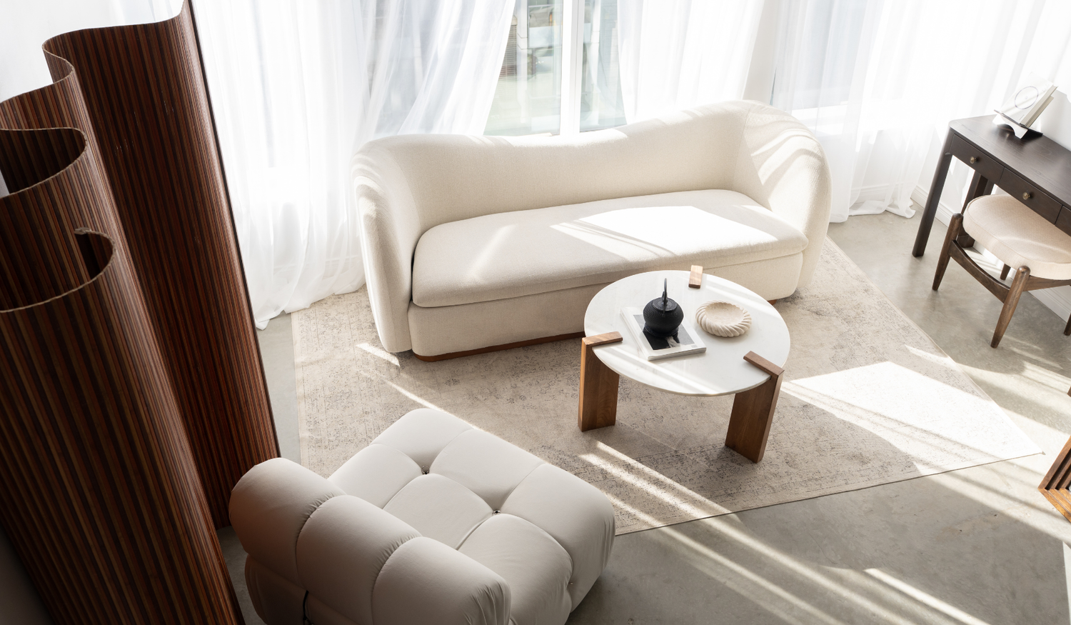 Sunlit cream sofa, round coffee table and sculptural chair beside a wood divider.