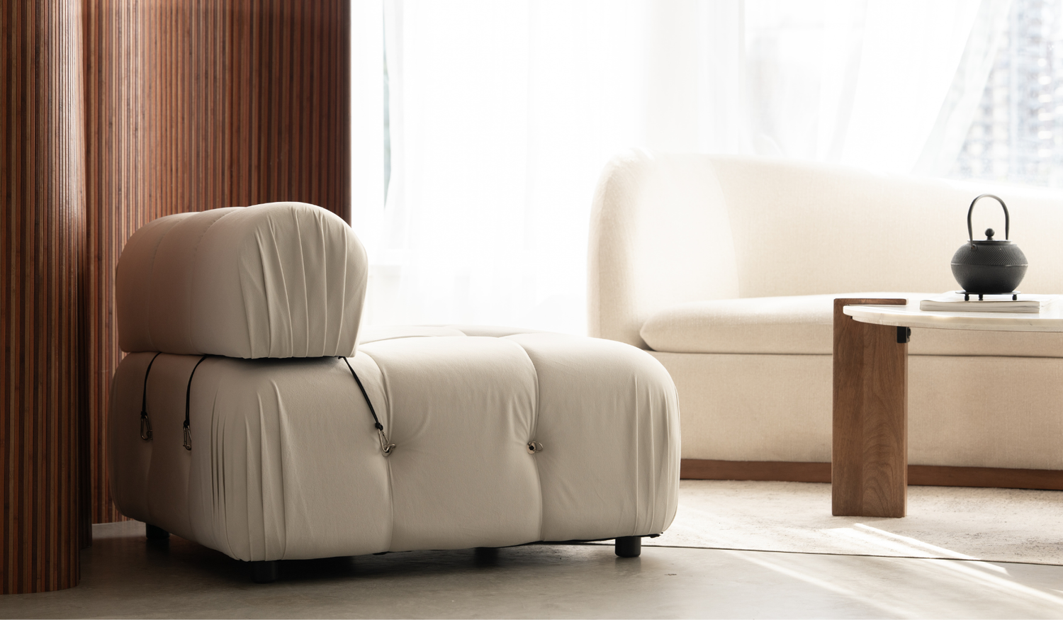 Sculptural cream chair beside the sofa and round coffee table.