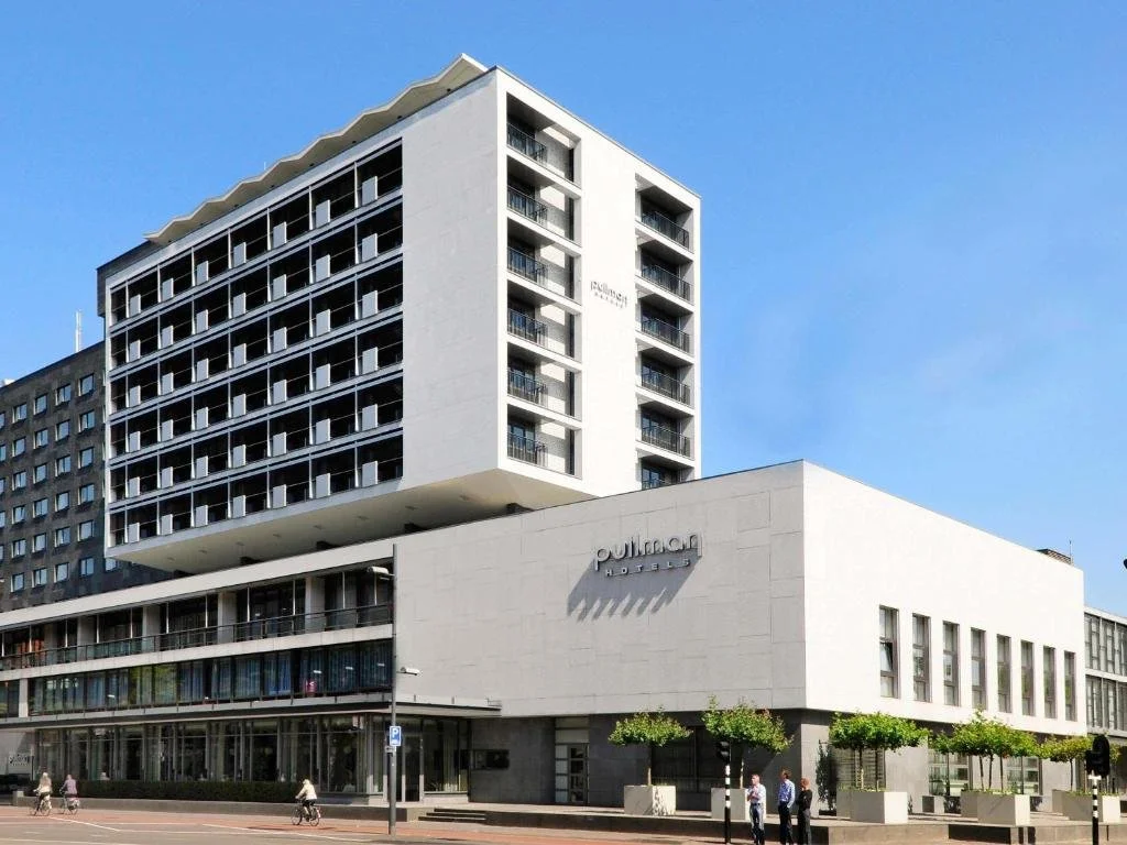 ein großes weißes Gebäude, vor dem Menschen entlanggehen in der Unterkunft Pullman Eindhoven Cocagne in Eindhoven