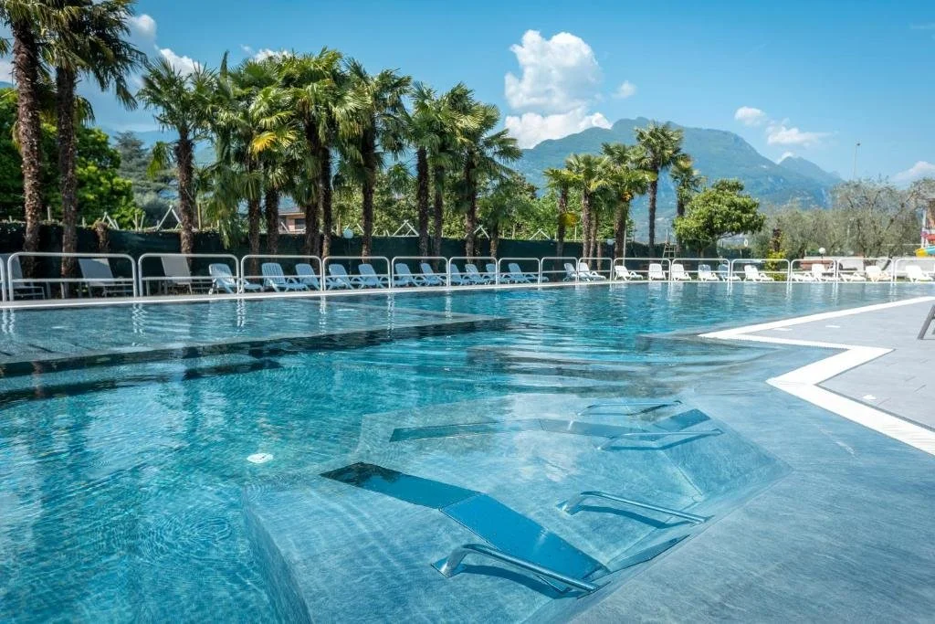 ein großer Swimmingpool mit Liegestühlen und Palmen in der Unterkunft Residence Filanda in Riva del Garda