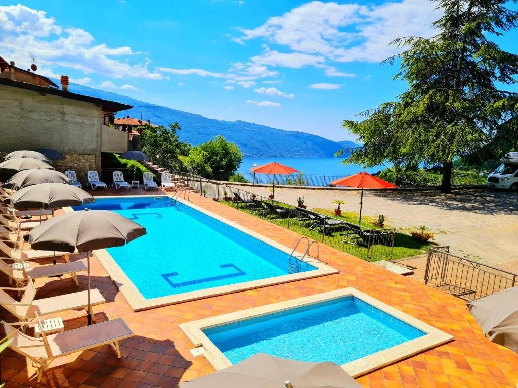 ein Swimmingpool mit Liegestühlen und Sonnenschirmen neben einem Ferienresort in der Unterkunft Residence Casa Silvana in Tignale