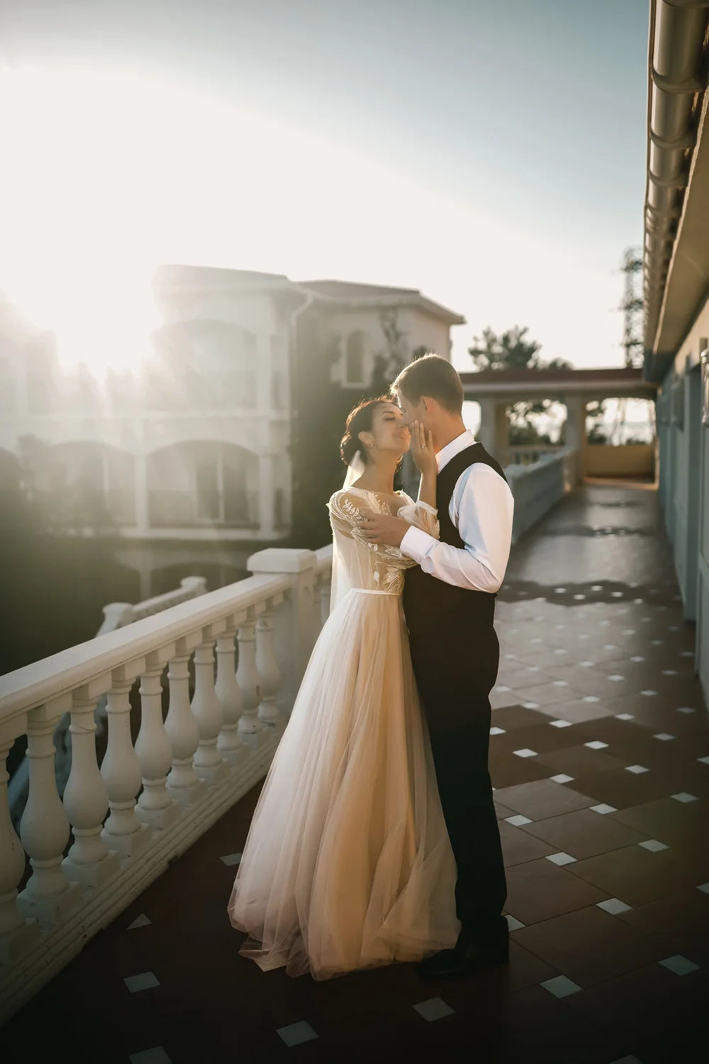 Couple embracing on a sunlit terrace beside a white balustrade.