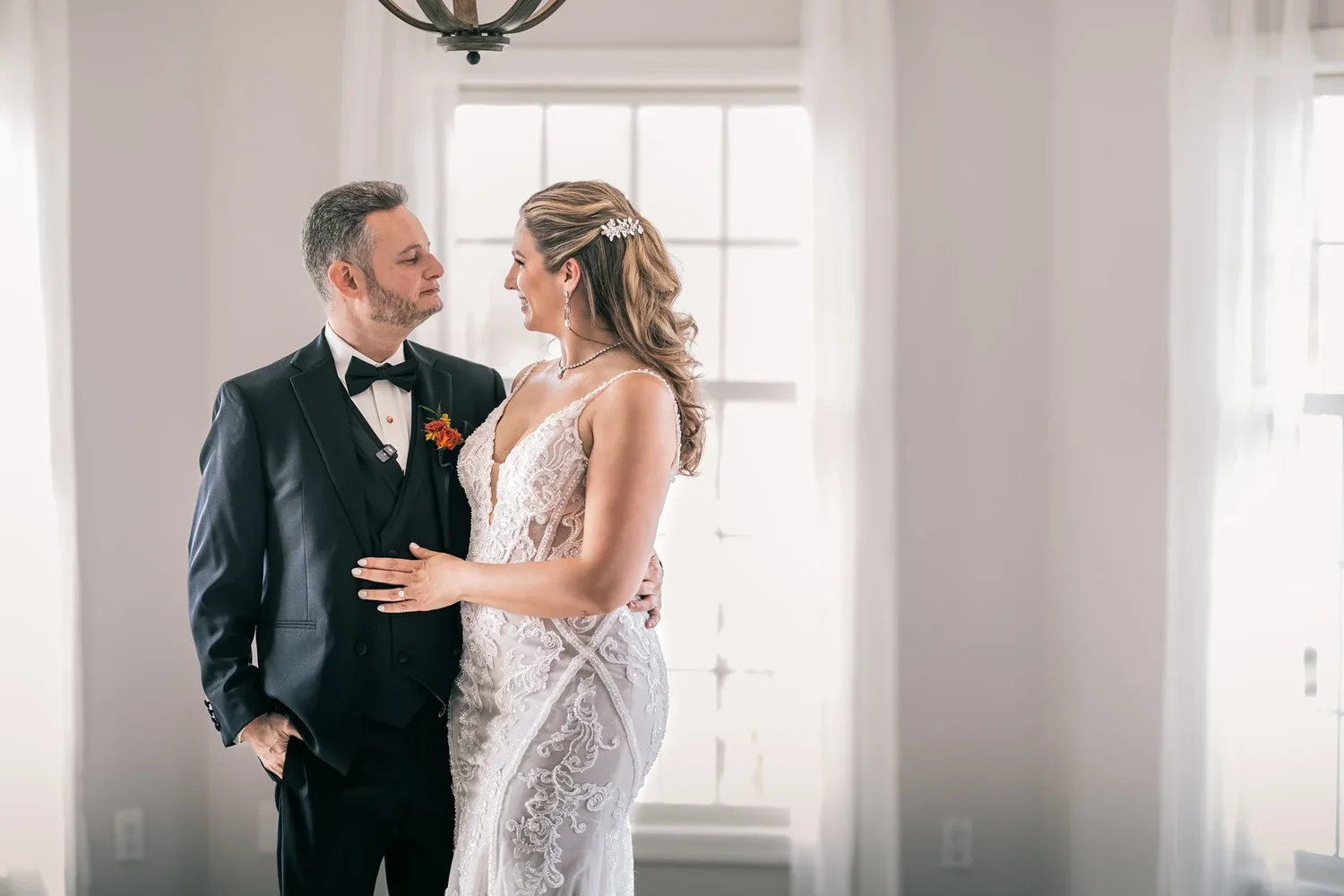 Charissa and Andrew smiling at each other in soft window light in the Manor House at Windham Manor, the frame filled by the two of them