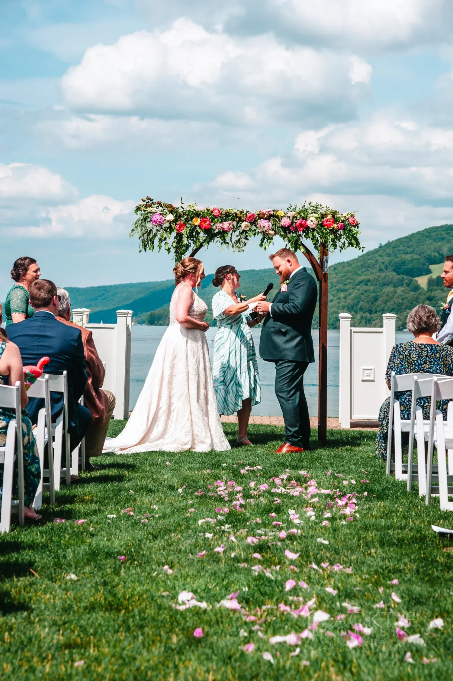 Amanda and Chris at a flower-covered ceremony arbor on the lawn above Otsego Lake at The Otesaga