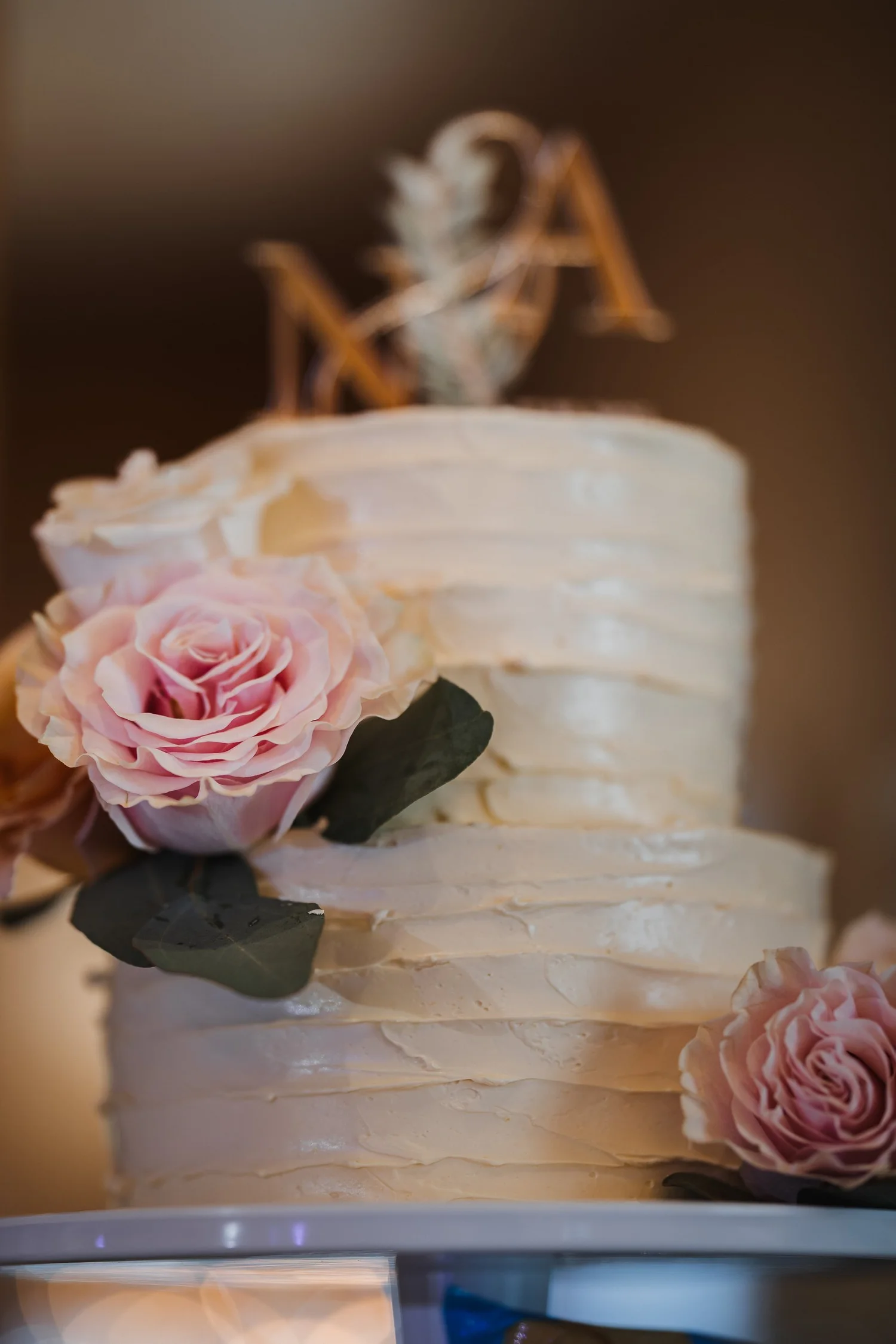 A white textured wedding cake with pink roses and a monogram topper