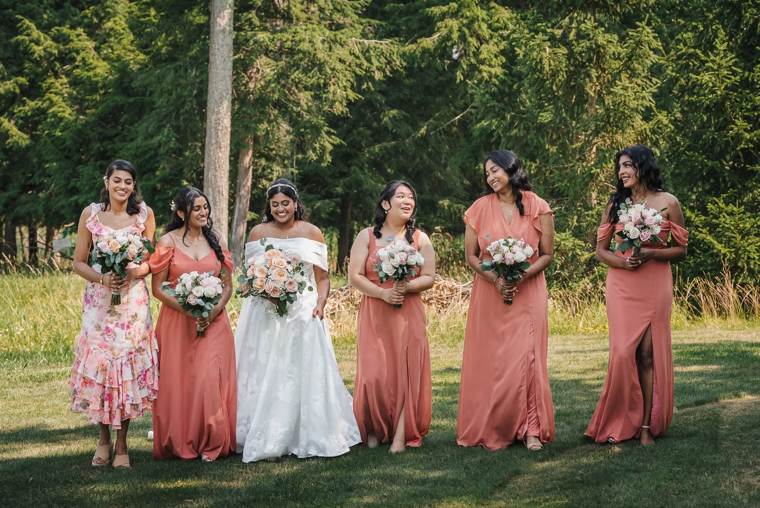 Natalia and her bridesmaids in coral dresses standing on a lawn with their bouquets
