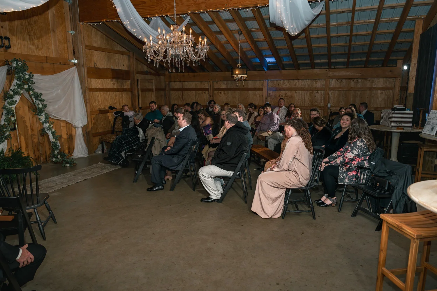 Guests seated for the ceremony inside the Black Barn, a crystal chandelier hanging from the wooden beams