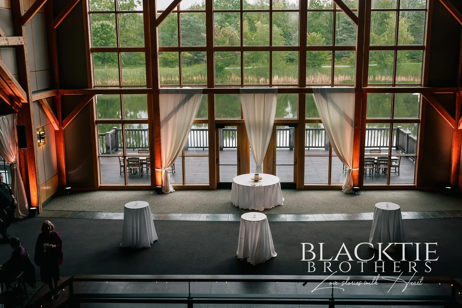 Cocktail tables in front of the window wall at Allyn Lodge, with the pond and trees visible through the glass.