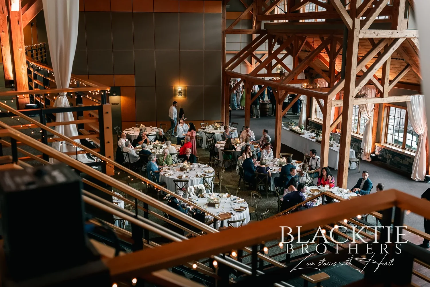 The great room at Allyn Lodge seen from the mezzanine, with the timber frame overhead and round tables set for dinner.