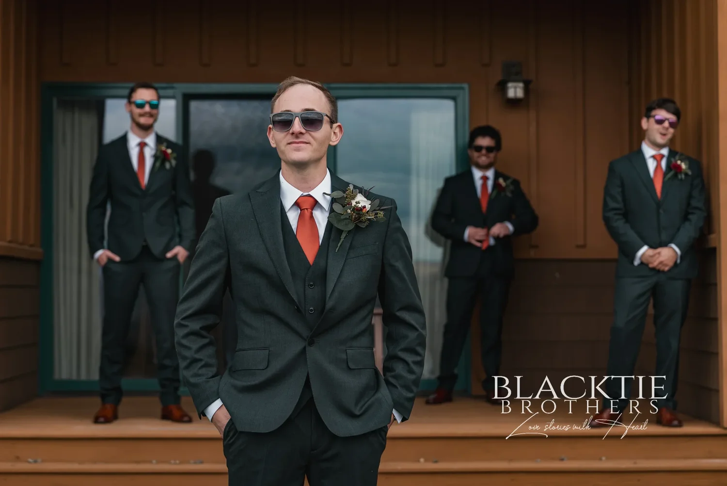 Gabe and his groomsmen in dark suits and copper ties on the deck of The Inn at Glenora, sunglasses on