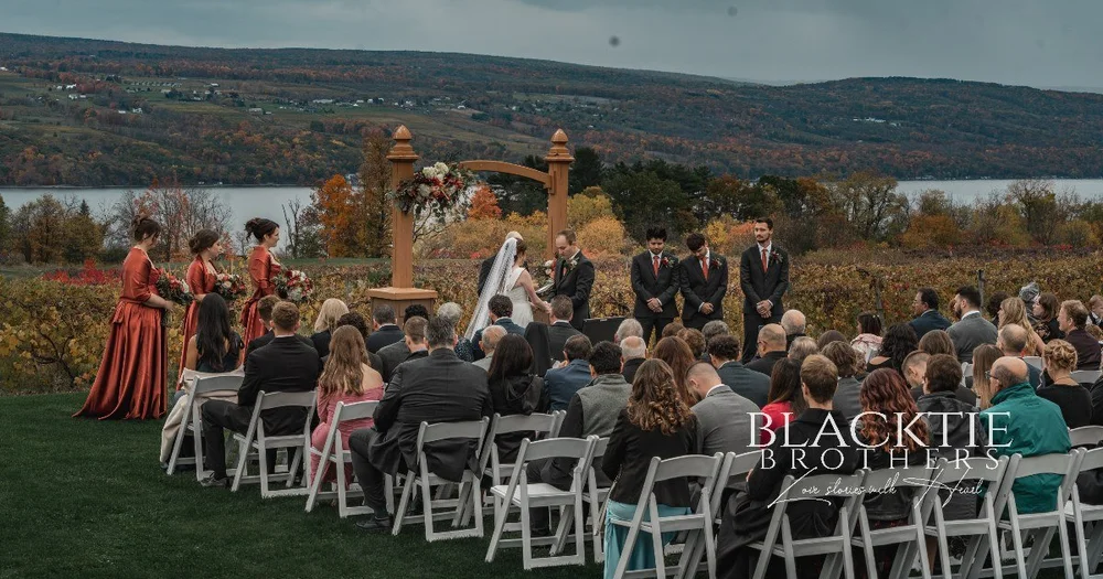 Wedding ceremony at the wooden arbor at Glenora Wine Cellars, guests seated on the lawn, with the vineyard and Seneca Lake behind