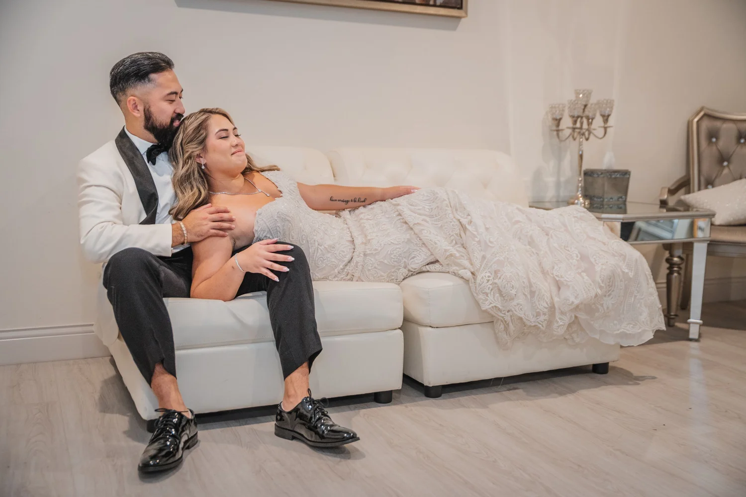 Mitchell sitting on the white couch in the bridal suite with Alice stretched across his lap in her gown