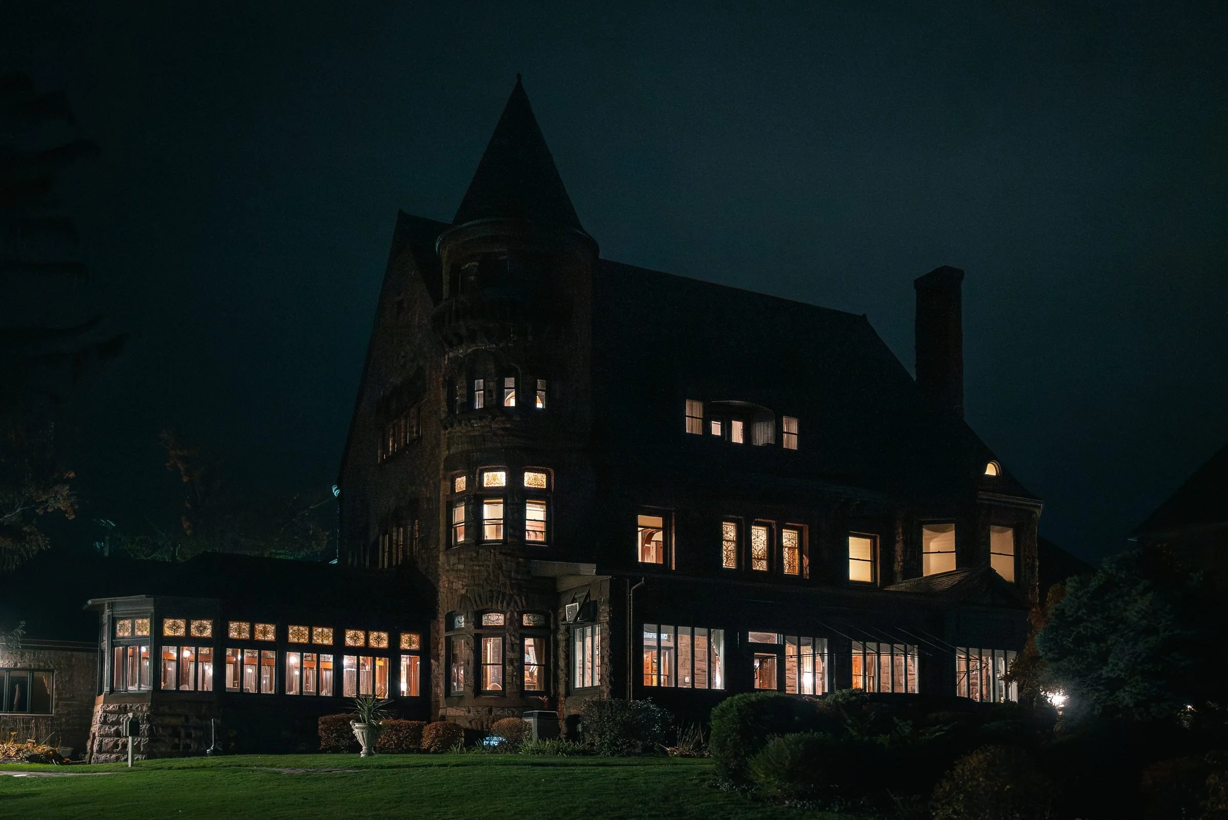 Belhurst Castle after dark, its stone turret against the night sky and warm light glowing from the windows and the long glass porch