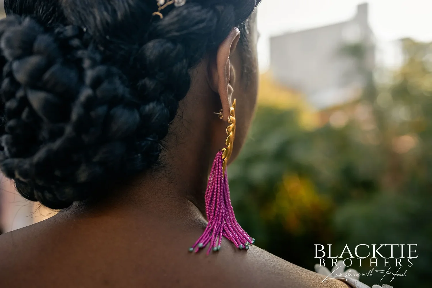 Close detail of Ciara's braided updo and a long fuchsia beaded earring against the soft green of the street