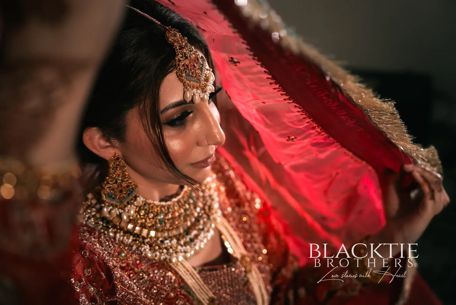 Jia lifting the edge of her red veil, seen in close profile with gold jewelry, in her room at the DoubleTree by Hilton Binghamton