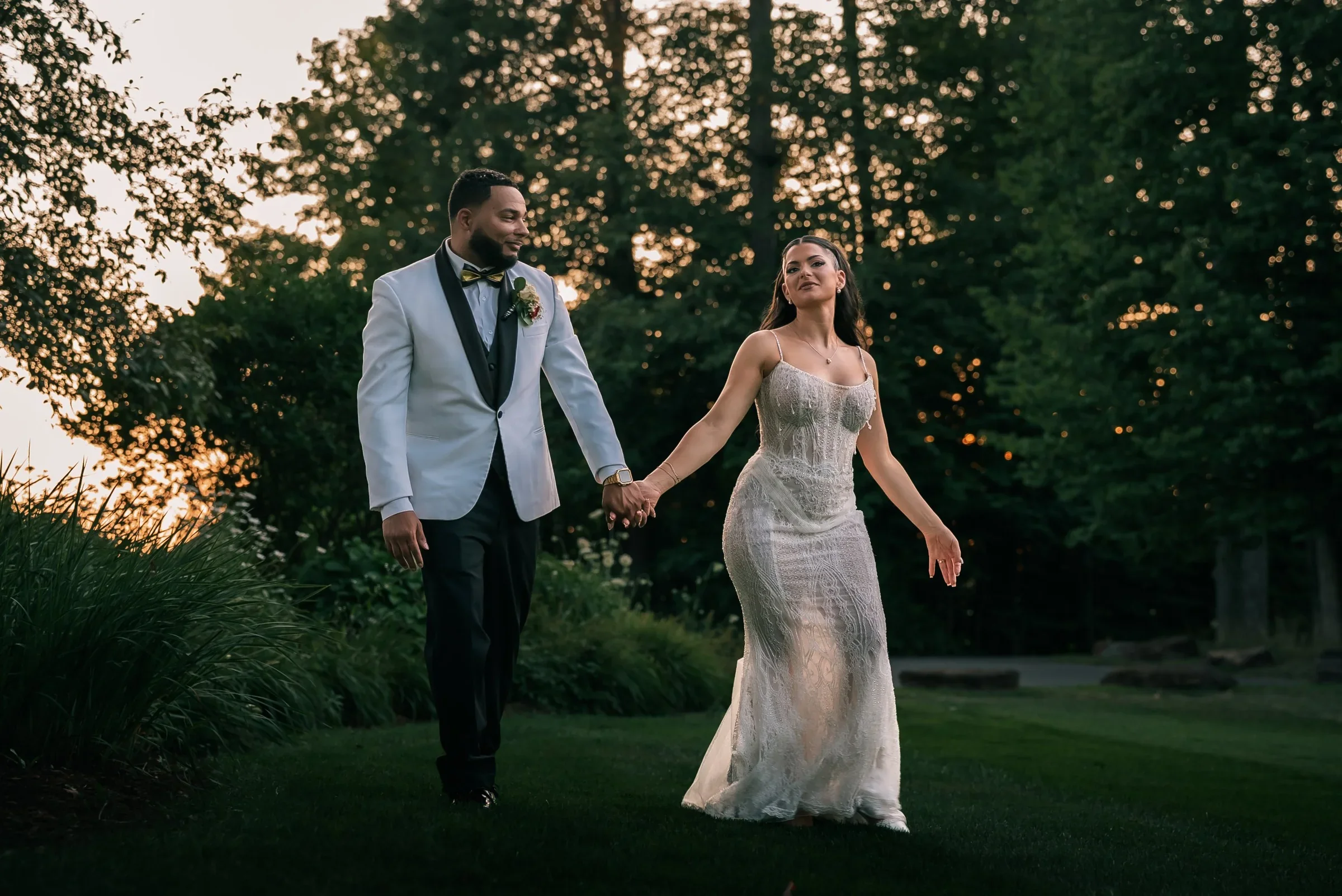 Vanessa and Trevor walking hand in hand across the lawn at sunset, Vanessa glancing toward the camera