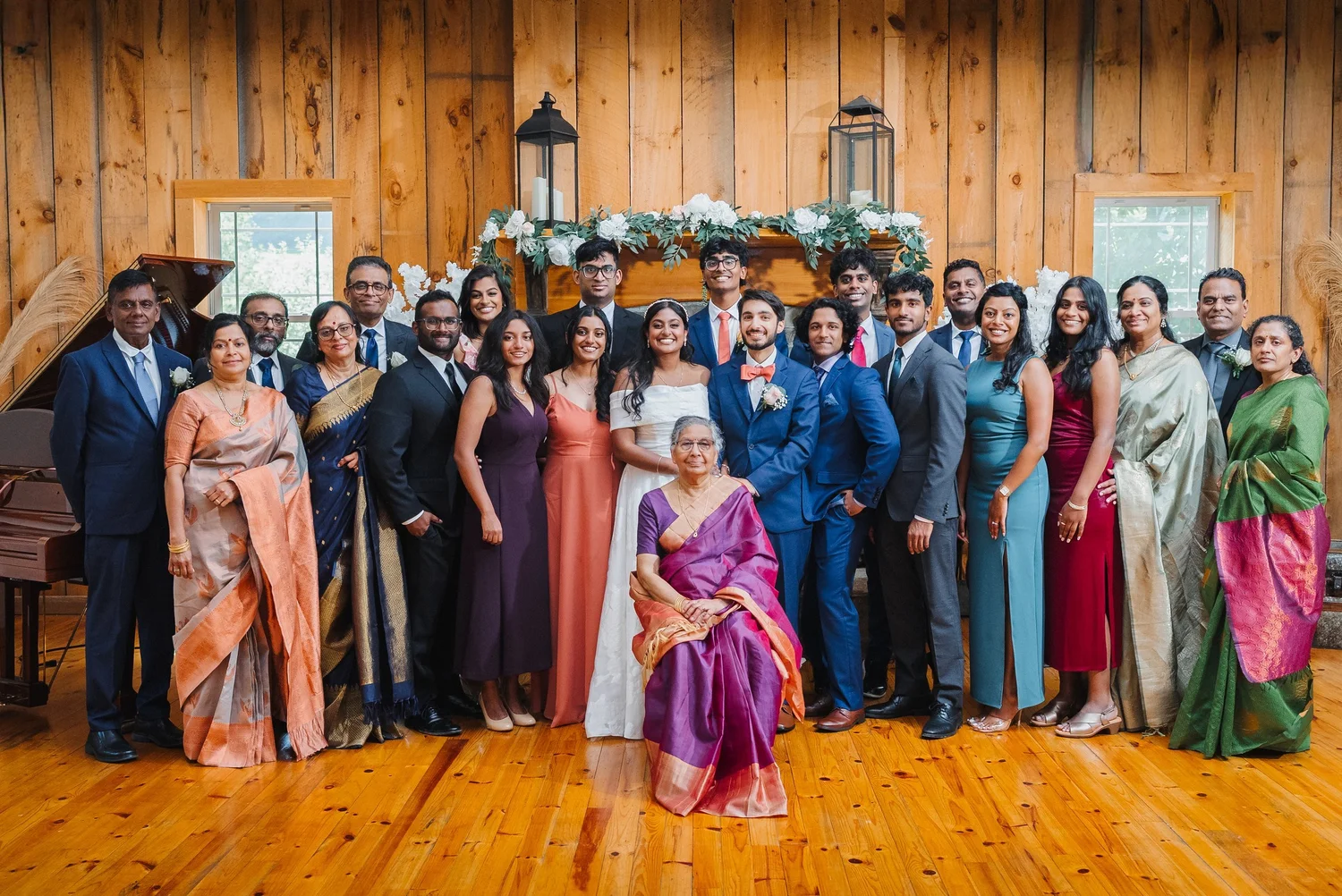 Natalia and Ansel with a large family group in suits, dresses and saris inside the wood-paneled barn