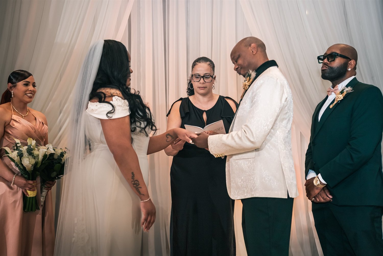 Tiffany and David exchange rings with their officiant and wedding party beside them.