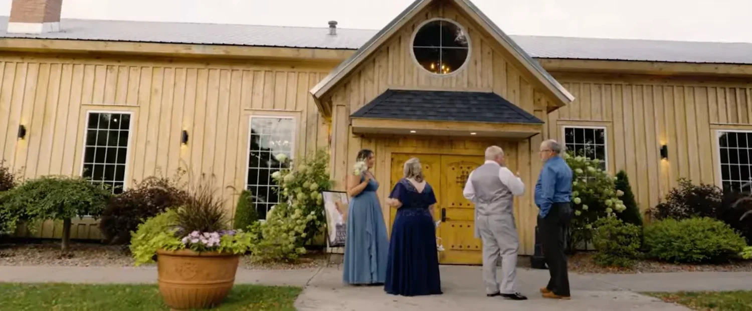 The entrance of The Cannery, a yellow barn with a round window above wooden double doors, with wedding guests gathered outside