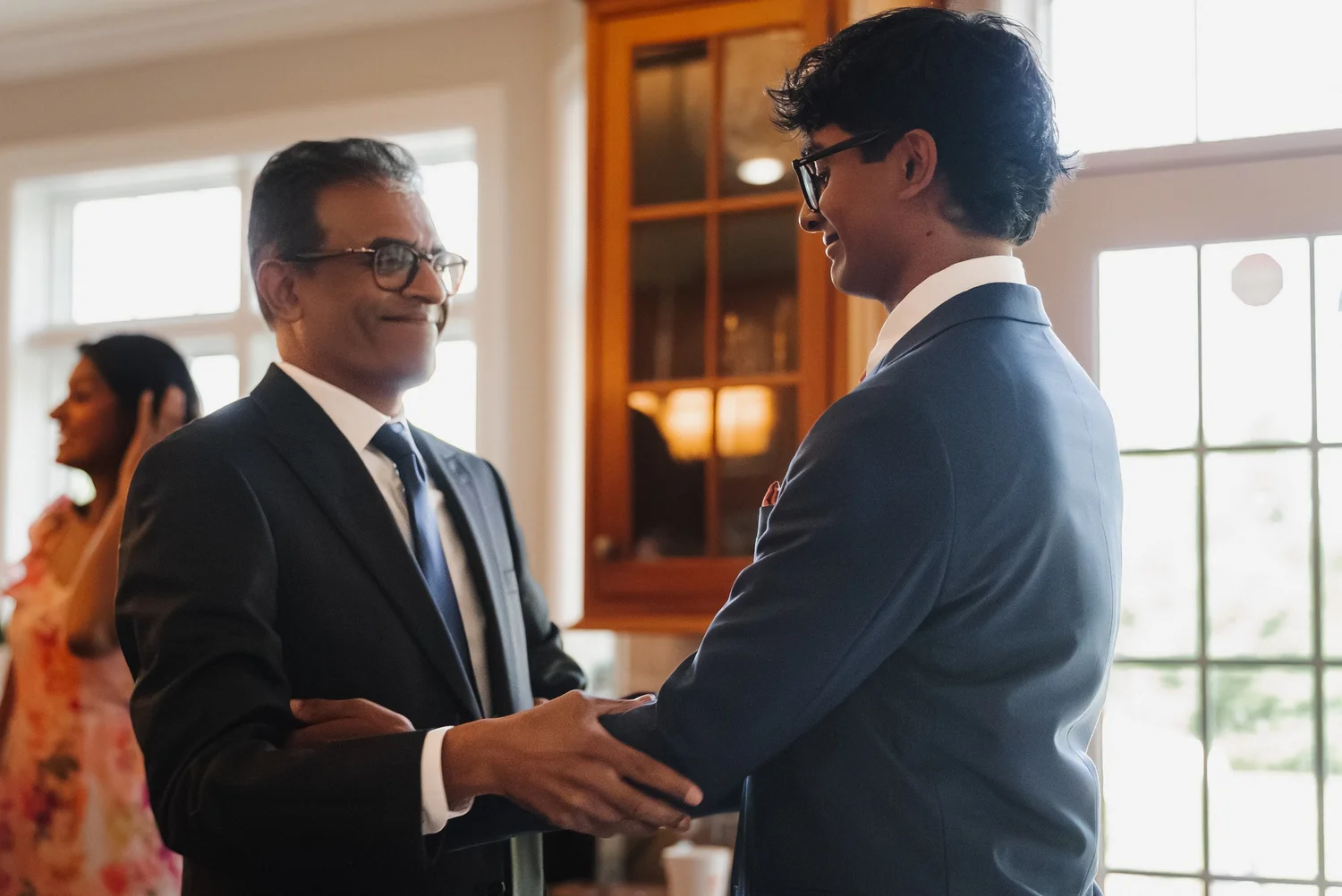 Ansel laughing with an older man in glasses while they get ready, both in dark suits