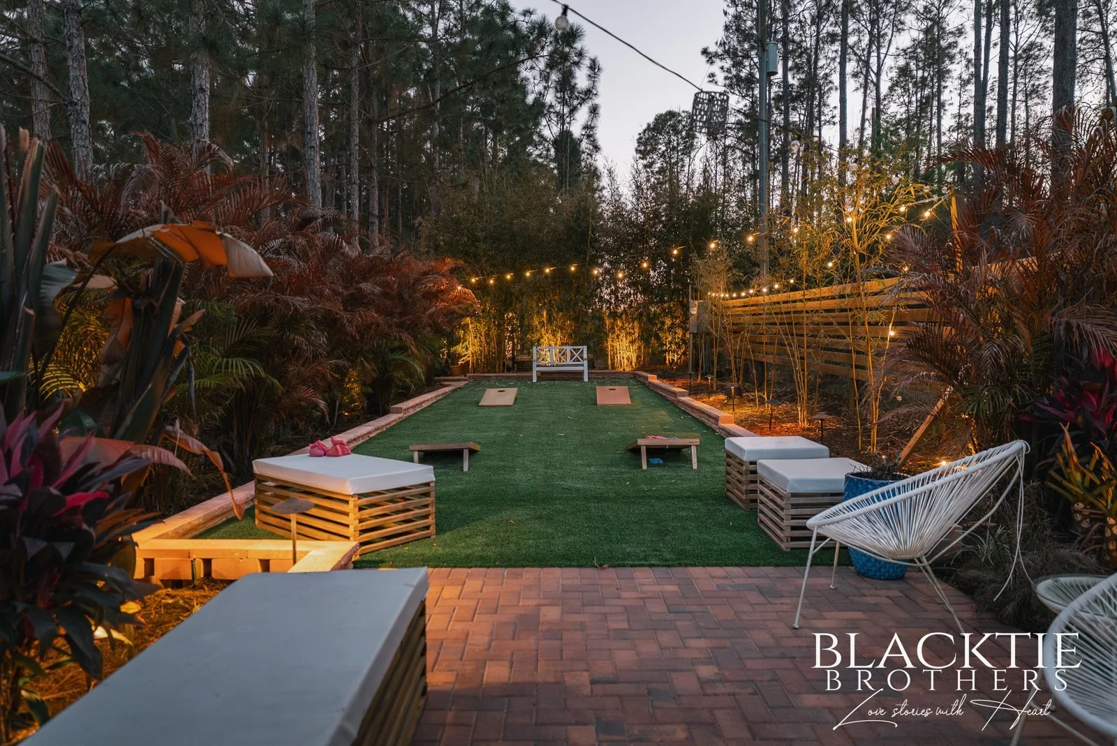 Low white lounge seating and chairs surround a green lawn among palms and glowing garden lights.