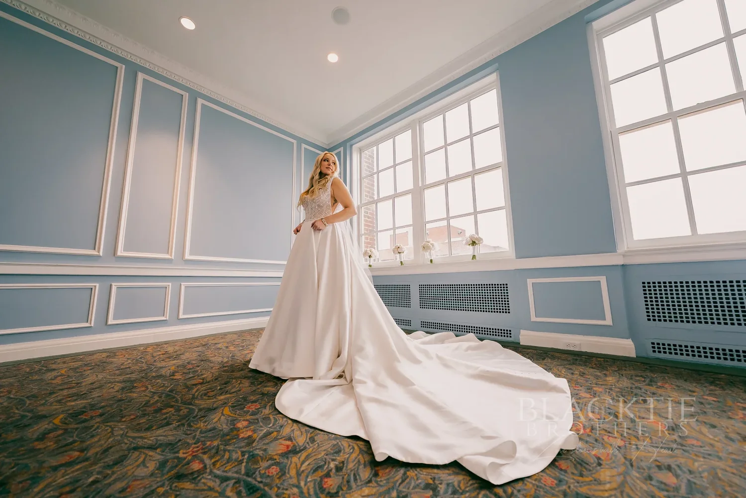 Catie in her gown in a blue-paneled room with tall windows at Marriott Syracuse Downtown